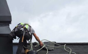 Homeowner inspecting gutters beside a shingled house in autumn with a ladder and fallen leaves.