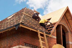 Person on a stable ladder attaching outdoor lights to a roof edge with protective clips