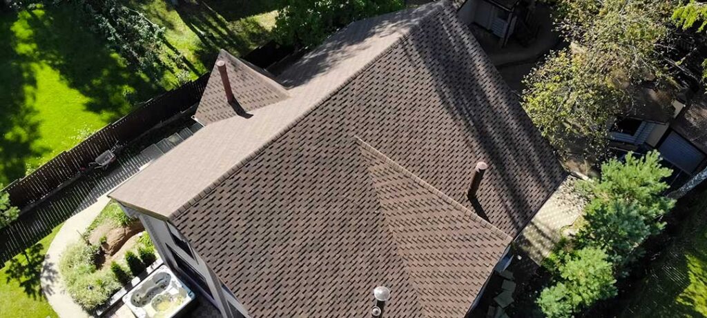 Homeowner examining shingles, flashing, and roof vents on a snow-season residential roof.