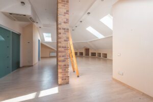 A homeowner examines evenly distributed attic insulation beside roof ventilation baffles and ceiling joists.